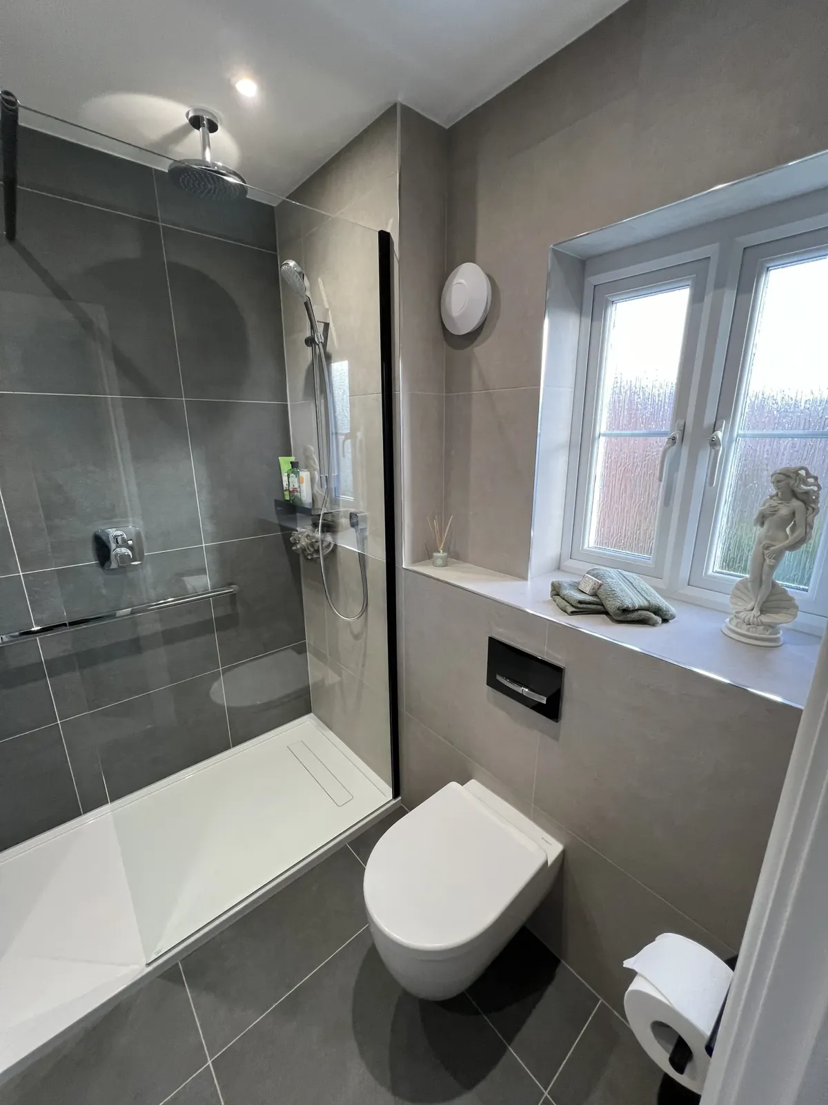 Walk-in shower area with a low-profile tray and linear drain in a beige tiled bathroom